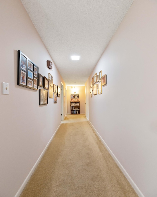 corridor with light carpet, a textured ceiling, and baseboards
