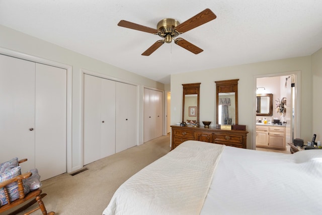 carpeted bedroom featuring two closets, ensuite bath, ceiling fan, and a textured ceiling