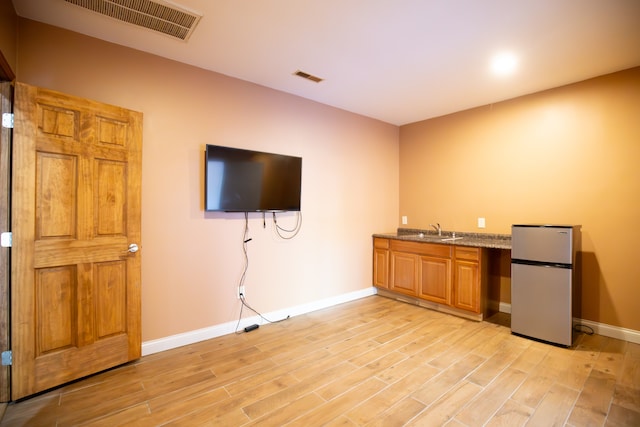 interior space featuring stainless steel refrigerator, light stone countertops, sink, and light hardwood / wood-style floors