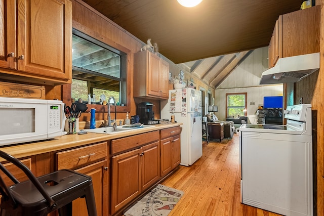 kitchen with light hardwood / wood-style floors, vaulted ceiling, white appliances, wood walls, and sink