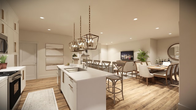 kitchen with white cabinets, a center island with sink, appliances with stainless steel finishes, sink, and decorative light fixtures