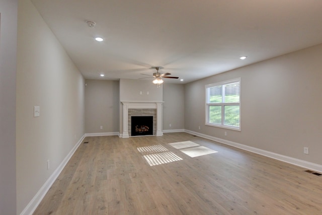 unfurnished living room with a tiled fireplace, light hardwood / wood-style flooring, and ceiling fan