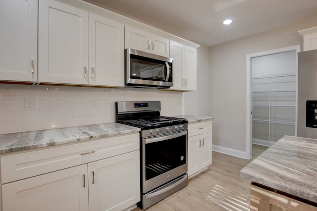 kitchen featuring light wood-type flooring, white cabinetry, decorative backsplash, appliances with stainless steel finishes, and light stone countertops