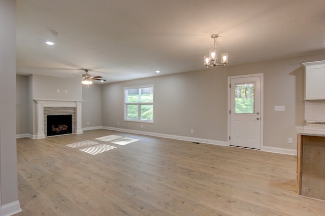 unfurnished living room with ceiling fan with notable chandelier, a fireplace, and light hardwood / wood-style flooring