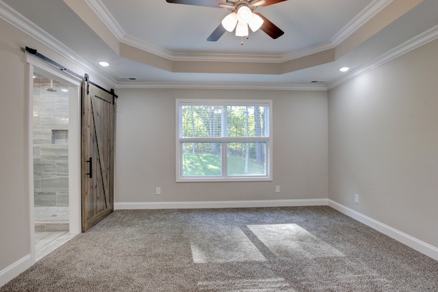 carpeted empty room featuring ceiling fan, ornamental molding, a raised ceiling, and a barn door