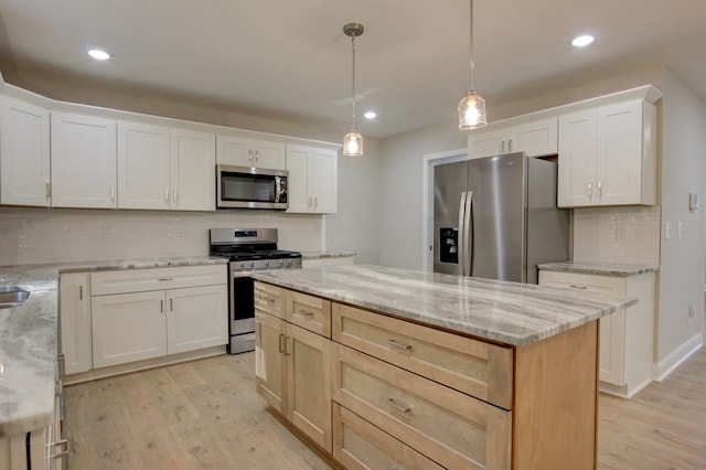 kitchen with white cabinets, pendant lighting, a kitchen island, appliances with stainless steel finishes, and light wood-type flooring