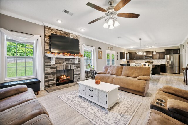 living room featuring crown molding, ceiling fan, a stone fireplace, and light hardwood / wood-style floors