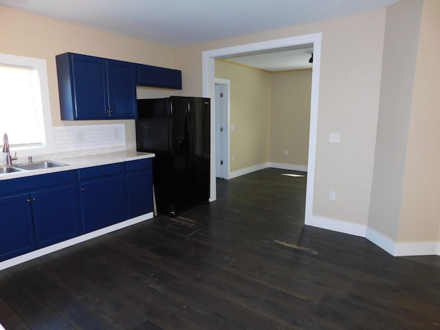 kitchen with sink, blue cabinetry, black refrigerator, dark hardwood / wood-style flooring, and decorative backsplash