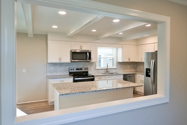 kitchen featuring appliances with stainless steel finishes, white cabinetry, sink, light stone counters, and beam ceiling