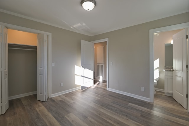 unfurnished bedroom featuring a closet, dark hardwood / wood-style flooring, crown molding, and ensuite bath