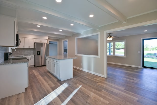 kitchen featuring ceiling fan, a kitchen island, beamed ceiling, white cabinetry, and stainless steel fridge