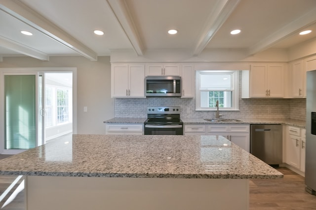 kitchen featuring white cabinetry, appliances with stainless steel finishes, beamed ceiling, a kitchen island, and sink