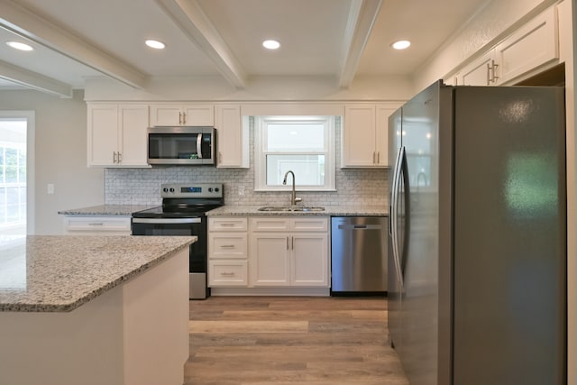 kitchen featuring appliances with stainless steel finishes, white cabinetry, light hardwood / wood-style floors, sink, and beam ceiling