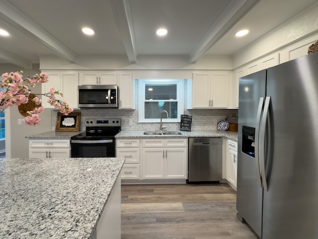 kitchen with appliances with stainless steel finishes, white cabinetry, tasteful backsplash, sink, and beam ceiling