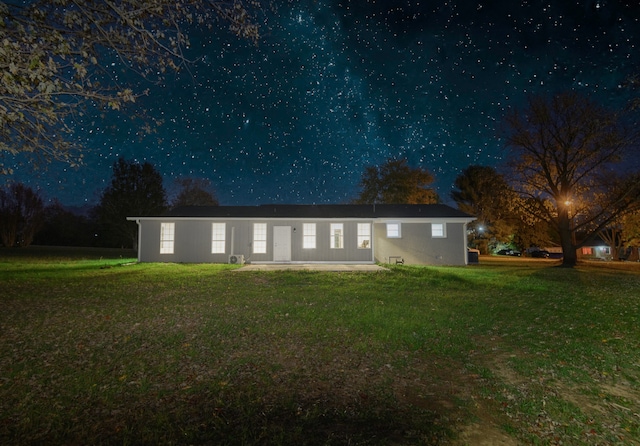 back house at night featuring a lawn