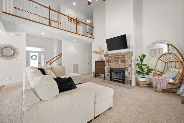 living room with a towering ceiling, ceiling fan, light colored carpet, and a stone fireplace