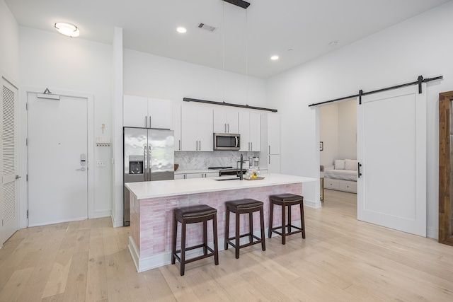 kitchen with a barn door, light hardwood / wood-style flooring, decorative light fixtures, white cabinets, and appliances with stainless steel finishes