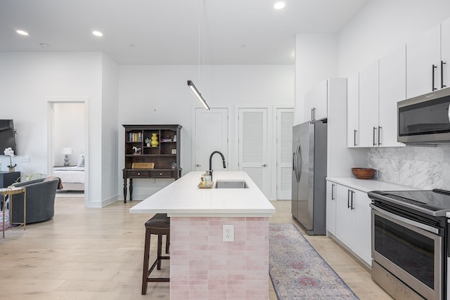 kitchen featuring an island with sink, sink, white cabinetry, light hardwood / wood-style flooring, and appliances with stainless steel finishes