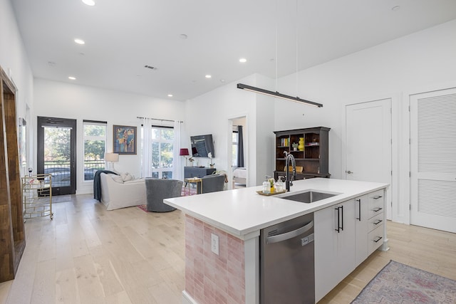 kitchen with white cabinets, sink, light hardwood / wood-style floors, a center island with sink, and dishwasher