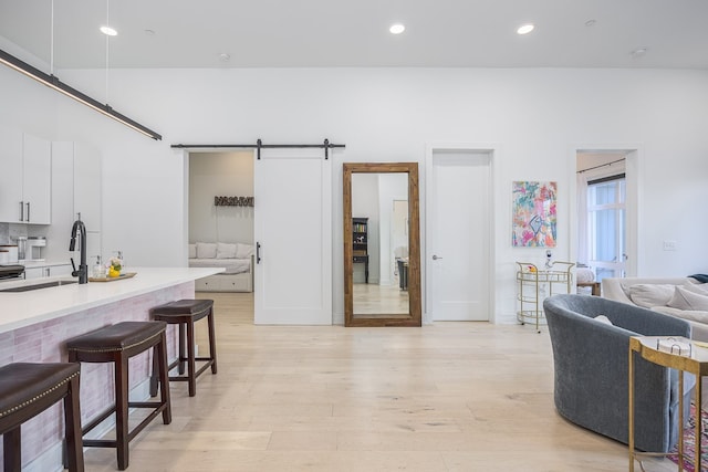 kitchen featuring a breakfast bar, sink, light hardwood / wood-style floors, white cabinetry, and a barn door