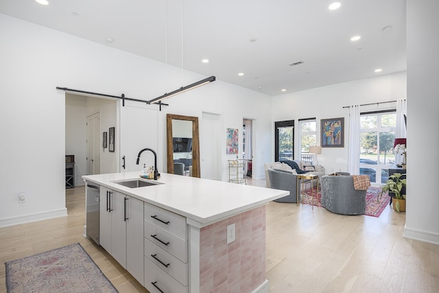 kitchen with an island with sink, sink, light hardwood / wood-style flooring, white cabinetry, and a barn door