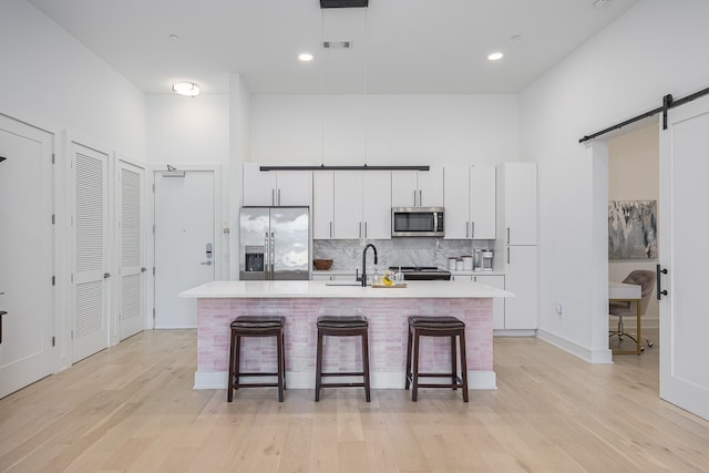 kitchen with an island with sink, stainless steel appliances, a breakfast bar, a barn door, and light hardwood / wood-style flooring