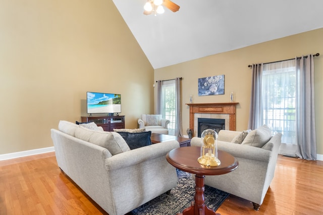 living room featuring high vaulted ceiling, ceiling fan, a tile fireplace, and light hardwood / wood-style floors