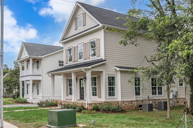 view of front of home featuring covered porch, a balcony, a front lawn, and central AC unit