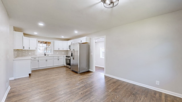 kitchen with backsplash, light wood-type flooring, stainless steel appliances, sink, and white cabinetry