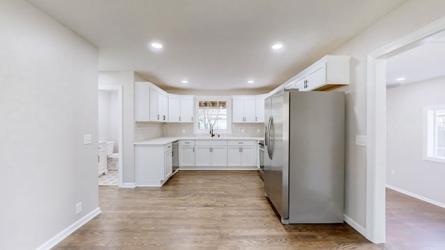 kitchen featuring backsplash, sink, stainless steel fridge, light wood-type flooring, and white cabinetry