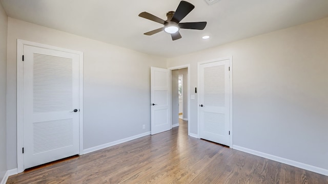 unfurnished bedroom with two closets, hardwood / wood-style flooring, and ceiling fan