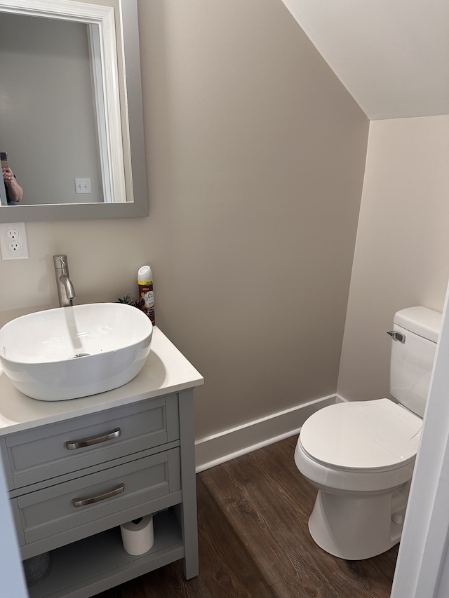 bathroom with wood-type flooring, vanity, lofted ceiling, and toilet