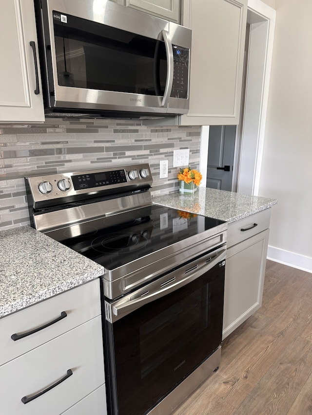 kitchen featuring light stone counters, tasteful backsplash, white cabinetry, appliances with stainless steel finishes, and light hardwood / wood-style floors