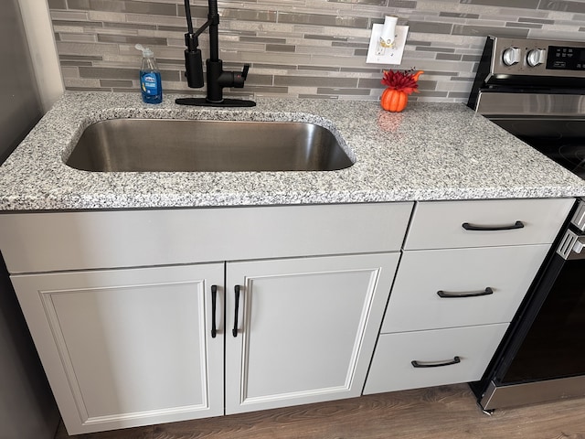 kitchen with electric range, sink, light stone counters, and white cabinetry