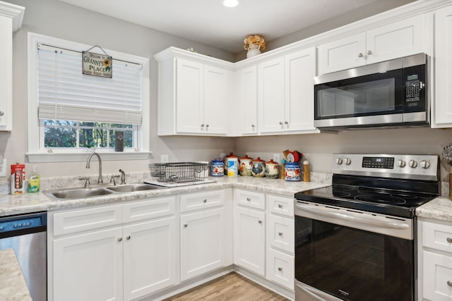 kitchen featuring light stone counters, white cabinets, sink, light hardwood / wood-style flooring, and stainless steel appliances