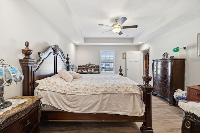 bedroom with a raised ceiling, ceiling fan, and light hardwood / wood-style flooring