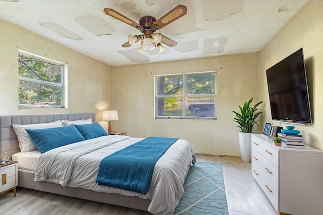 bedroom with multiple windows, a textured ceiling, ceiling fan, and light hardwood / wood-style flooring