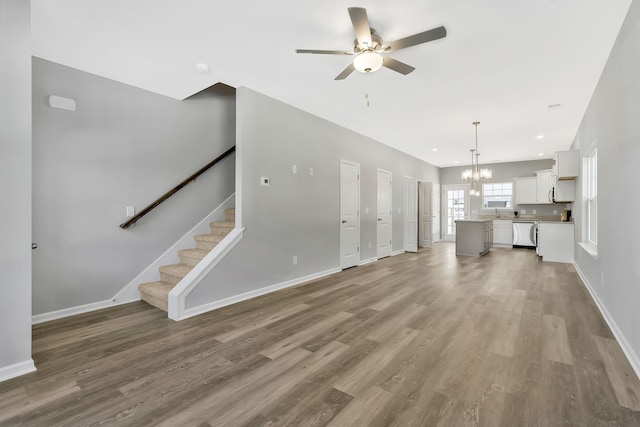 unfurnished living room featuring wood-type flooring and ceiling fan with notable chandelier