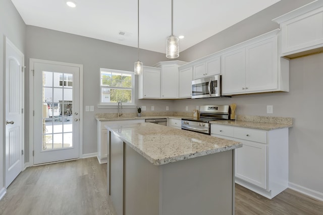 kitchen with appliances with stainless steel finishes, light hardwood / wood-style floors, white cabinetry, a center island, and decorative light fixtures