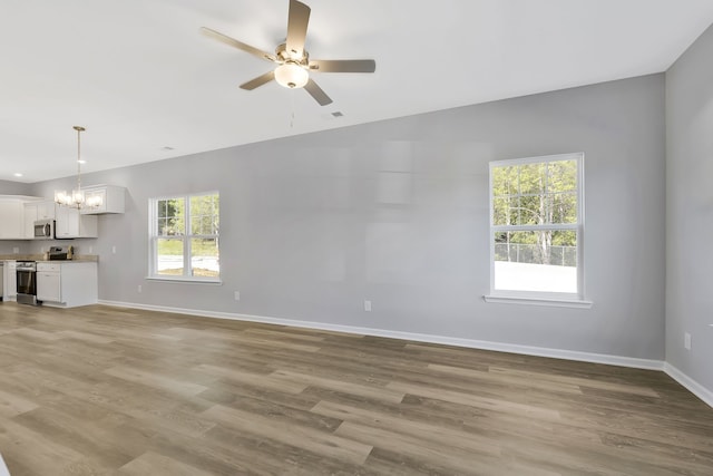 unfurnished living room featuring ceiling fan with notable chandelier, light hardwood / wood-style flooring, and plenty of natural light