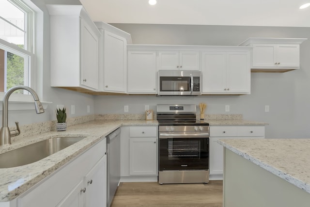 kitchen with light hardwood / wood-style floors, light stone counters, white cabinets, stainless steel appliances, and sink