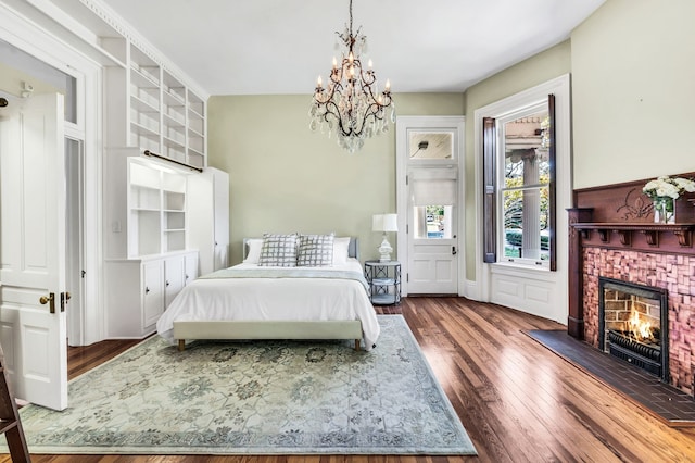 bedroom featuring a brick fireplace, a notable chandelier, and dark hardwood / wood-style floors