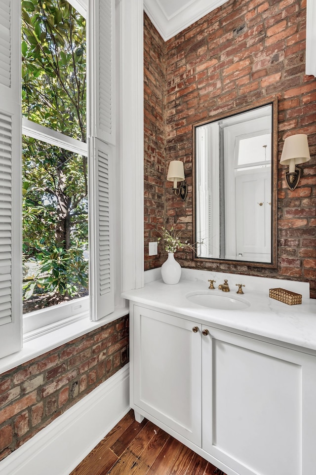 bathroom with hardwood / wood-style flooring, crown molding, vanity, and brick wall