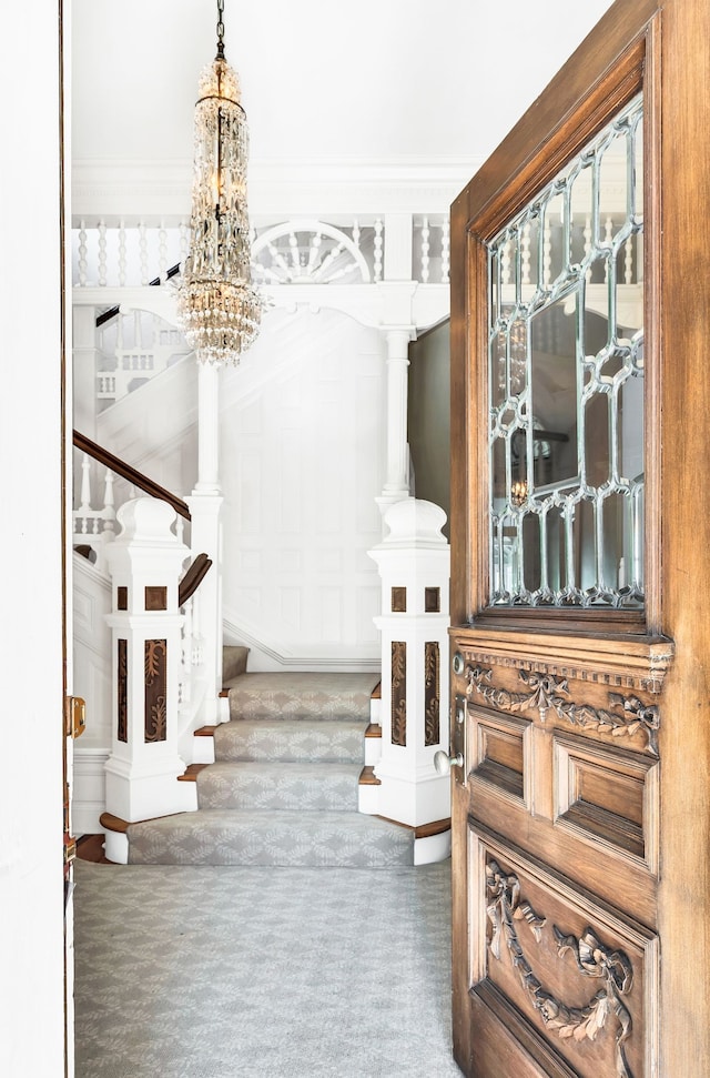 carpeted foyer entrance featuring ornamental molding and a chandelier