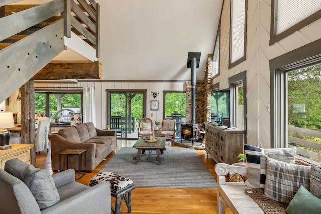 living room with light hardwood / wood-style floors, a towering ceiling, a wood stove, and a wealth of natural light