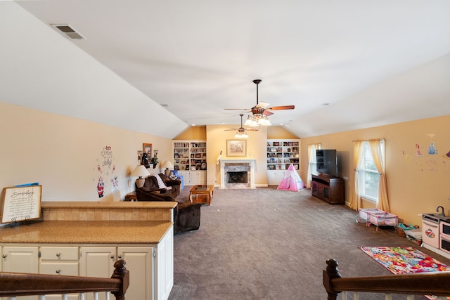 living room with built in shelves, carpet flooring, vaulted ceiling, a premium fireplace, and ceiling fan