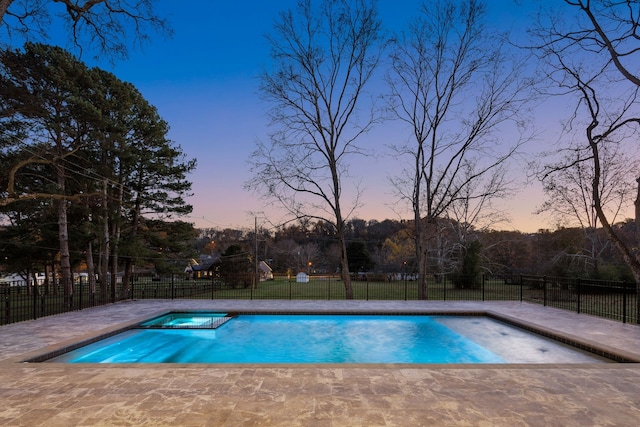 pool at dusk featuring an in ground hot tub and a patio