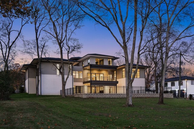 back house at dusk with a balcony and a yard