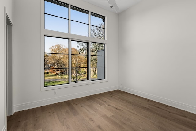 spare room featuring a wealth of natural light, hardwood / wood-style floors, a towering ceiling, and ceiling fan