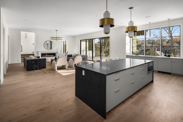 kitchen with stainless steel microwave, a center island, light hardwood / wood-style flooring, decorative light fixtures, and gray cabinets